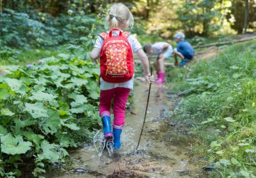 Wandern mit Kindern - Kleines Mädchen läuft mit ihrem Rucksack in einem Flussbett.