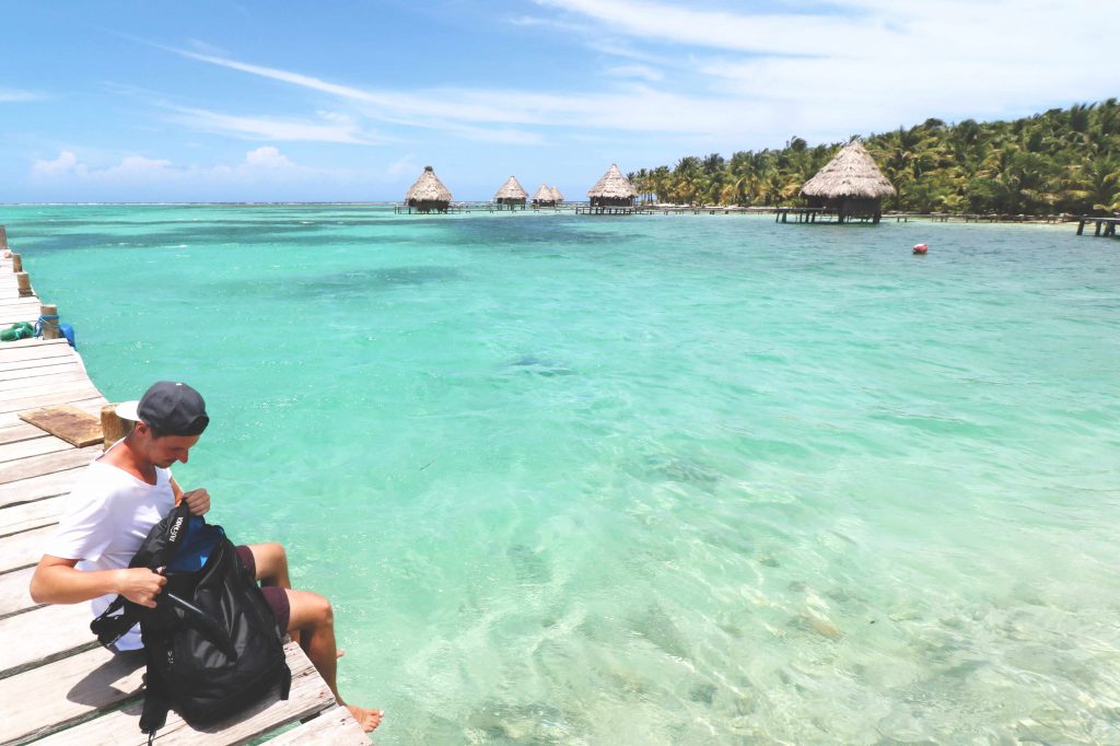 Daniel sitzt auf einem Steg der Insel Laughing Bird Caye vor der Küste von Belize und blickt auf das glasklare Wasser.