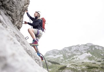 Via ferrata to the sky 18 Via ferrata - Woman with a red backpack and a white helmet climbing a via ferrata.